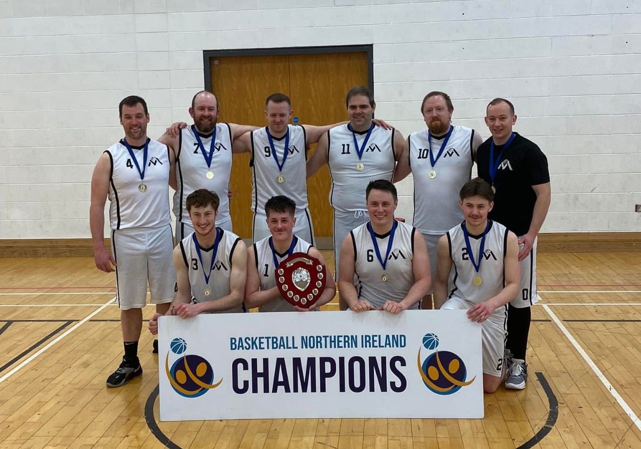 The Mourne senior men with their medals and a shield, kneeling behind a Basketball Northern Ireland Champions banner